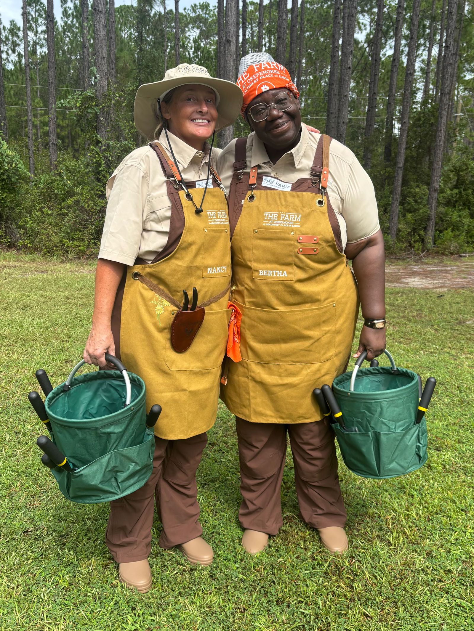 Nancy and Bertha in farm aprons, holding garden tool buckets, at The Farm at Okefenokee